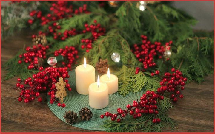 White candles surrounded by cranberries and pine branches - creating a cozy hygge Christmas