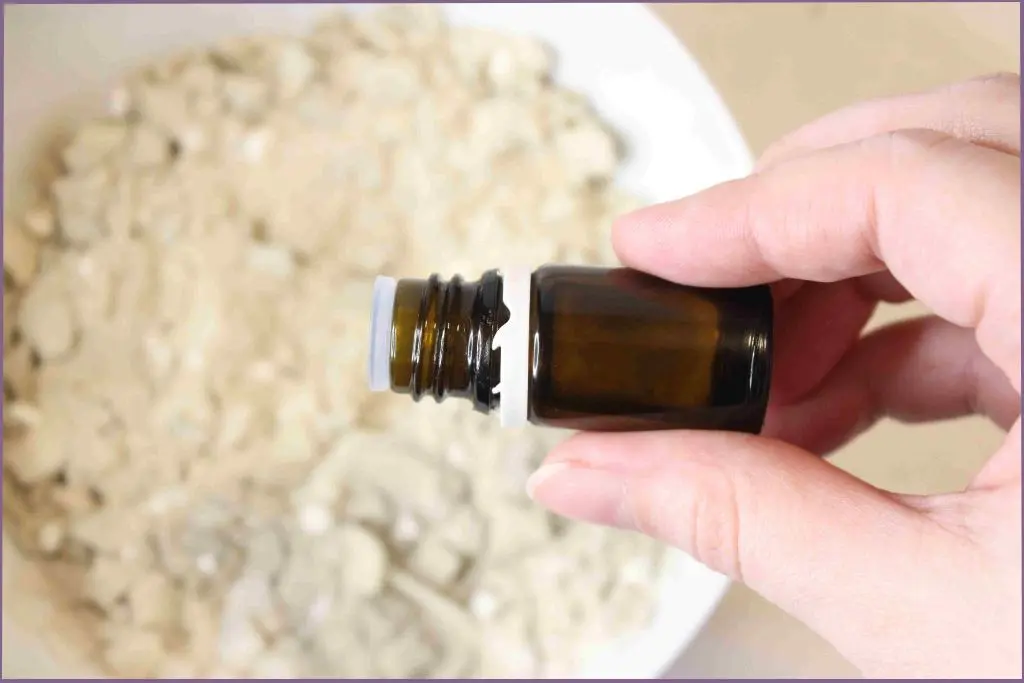 adding essential oil from a bottle to bentonite clay detox bath powder in a bowl