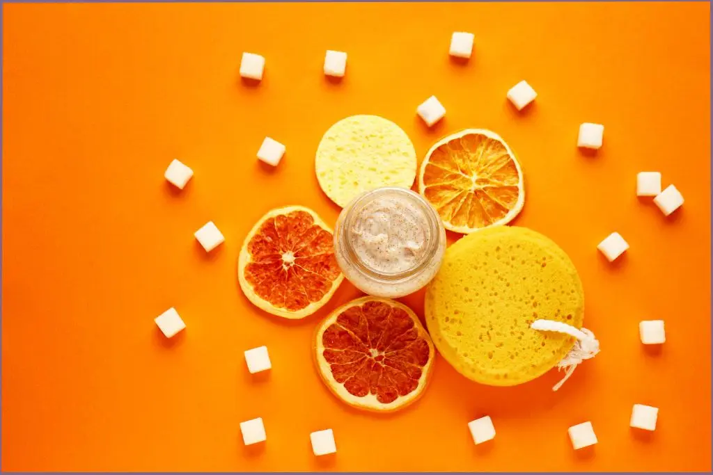 sugar scrub on orange background surrounded by sugar cubes and lime slices