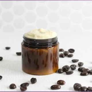 homemade coffee eye cream in amber glass jar with coffee beans scattered around table