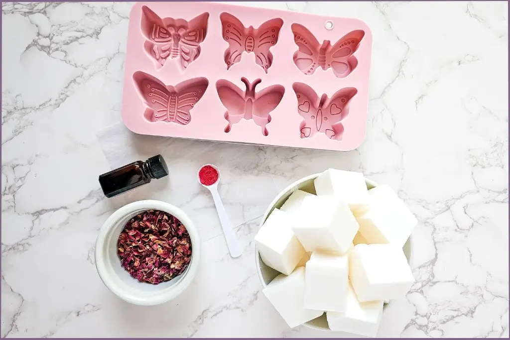 butterfly shaped soap molds, rose petals in bowl, melt and pour soap pieces and essential oil bottle - ingredients for soap making