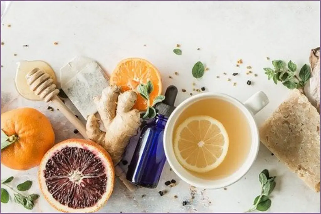 blue bottle of essential oil surrounded by lemon tea, grapefruit, ginger, and a honey stick