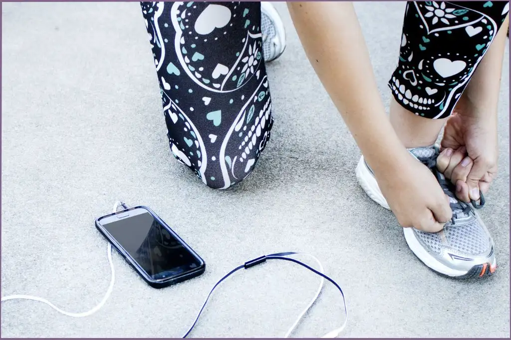 lady tying the laces on her running shoes with a phone lying on the floor