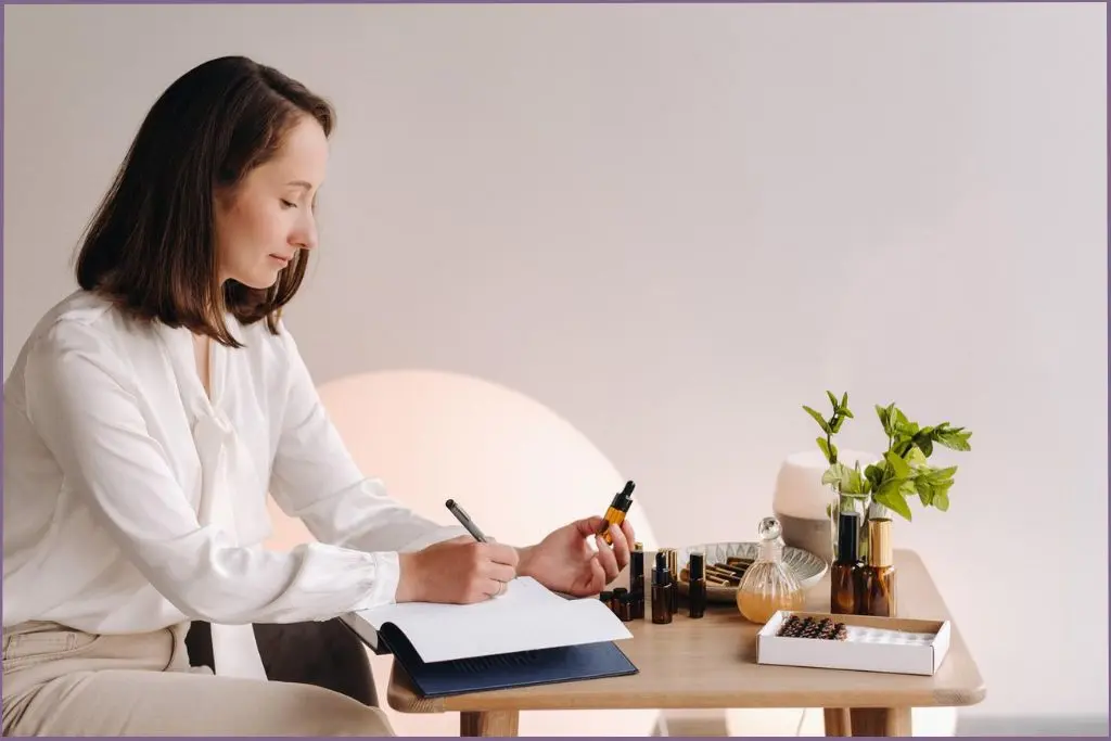 lady holding an essential oil bottle and writing in a book , researching the connection between essential oils and weight loss