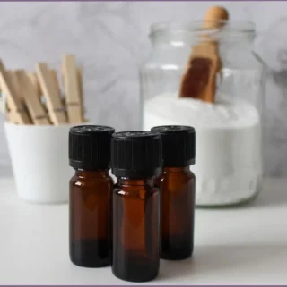 3 essential oil bottles in front of a jar of diatomaceous earth and a mug with clothes clips