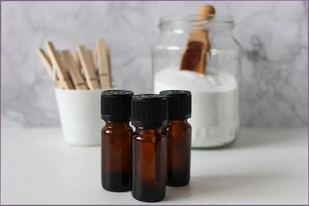 3 essential oil bottles in front of a jar of diatomaceous earth and a mug with clothes clips