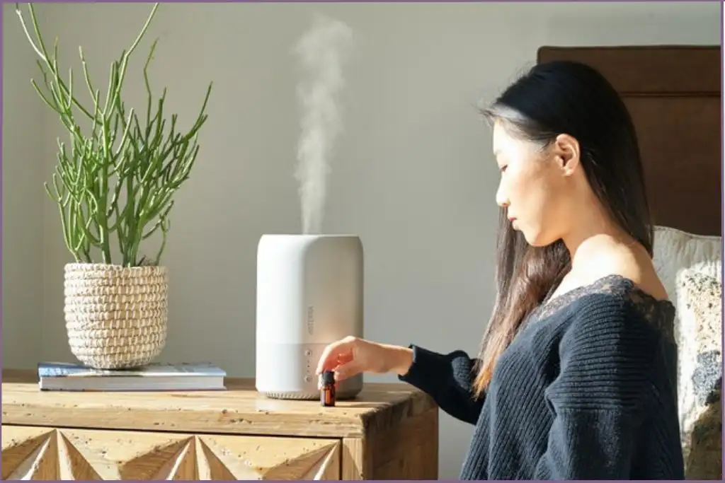 lady in bedroom touching essential oil bottle with a diffuser on the background