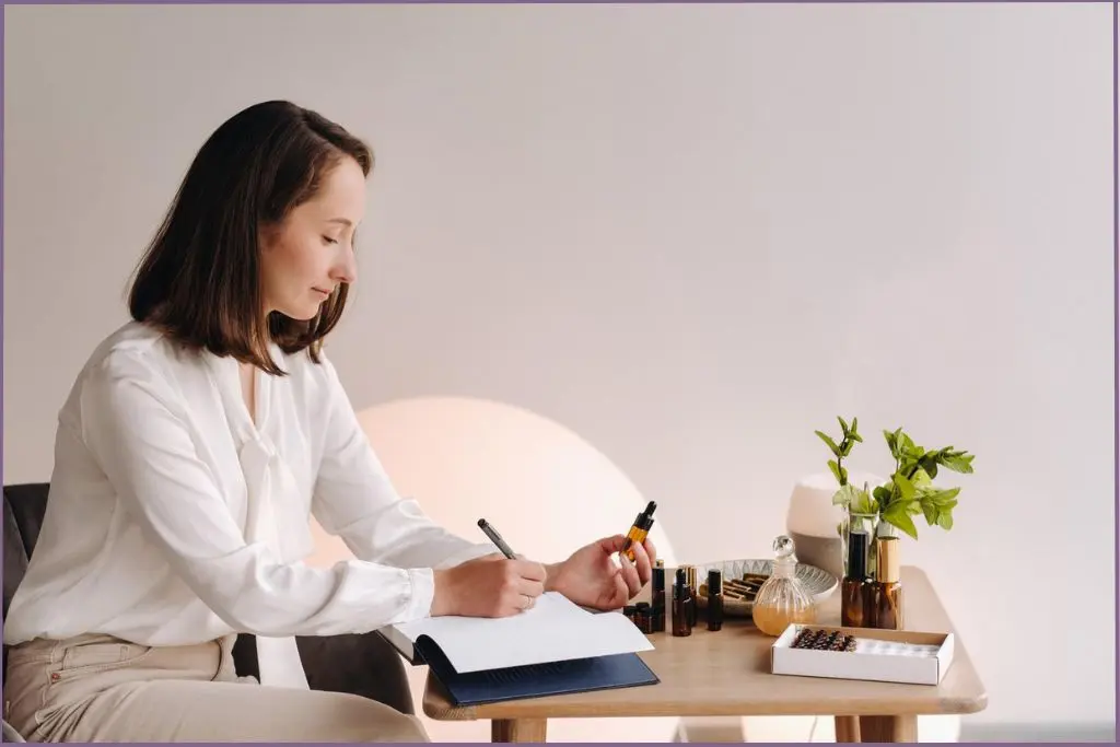 lady holding essential oil bottle in her hand and writing in a book