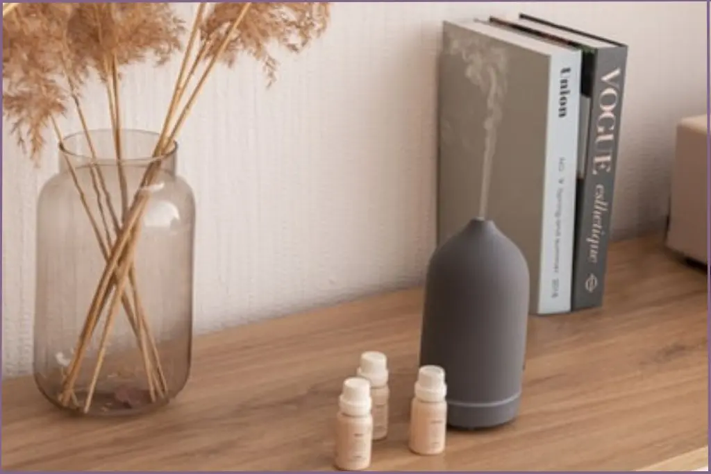 grey diffuser on a side table with 2 books and 3 essential oil bottles