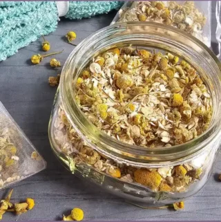 glass bottle and a mesh bag filled with chamomile and oatmeal for homemade herbal bath tea bags