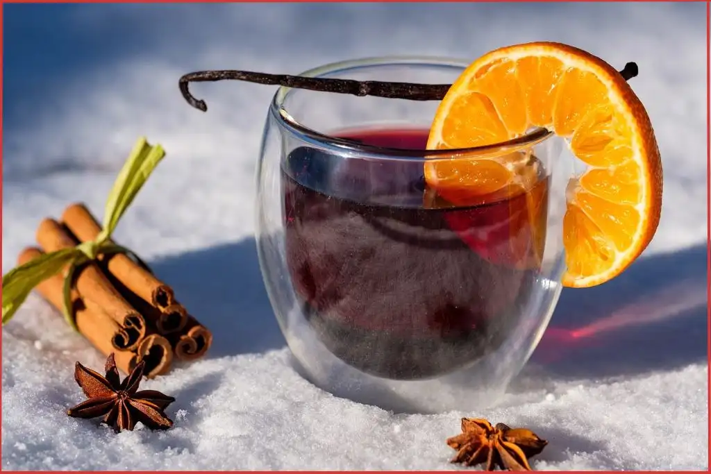 glass with mulled wine with vanilla pod across it and bundle of cinnamon sticks nearby