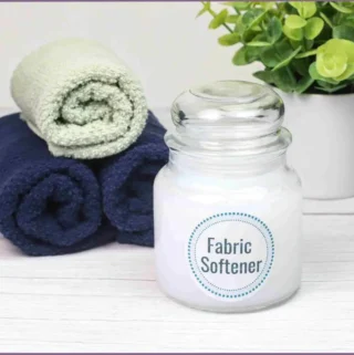 glass jar with homemade fabric softener and three rolled up towels in background