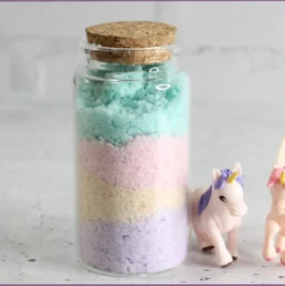 Pretty pastels bath salts recipe packed in glass jar with cork. Two plastic unicorns lay at the side of the bottle
