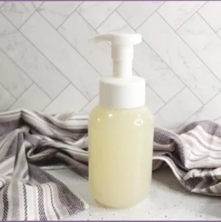 Pump bottle with homemade foaming hand soap recipe beside a purple striped dishtowel