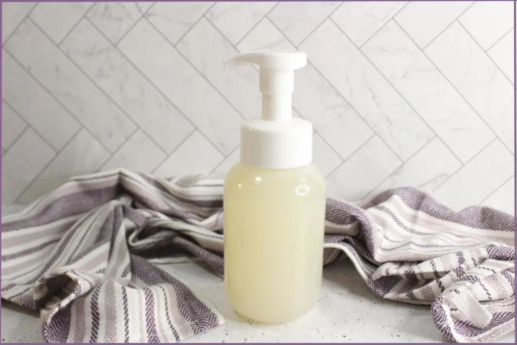 Pump bottle with homemade foaming hand soap recipe beside a purple striped dishtowel