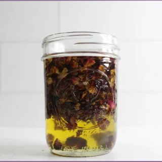 rose petals steeping in carrier oils in a glass bottle - how to make rose oil at home