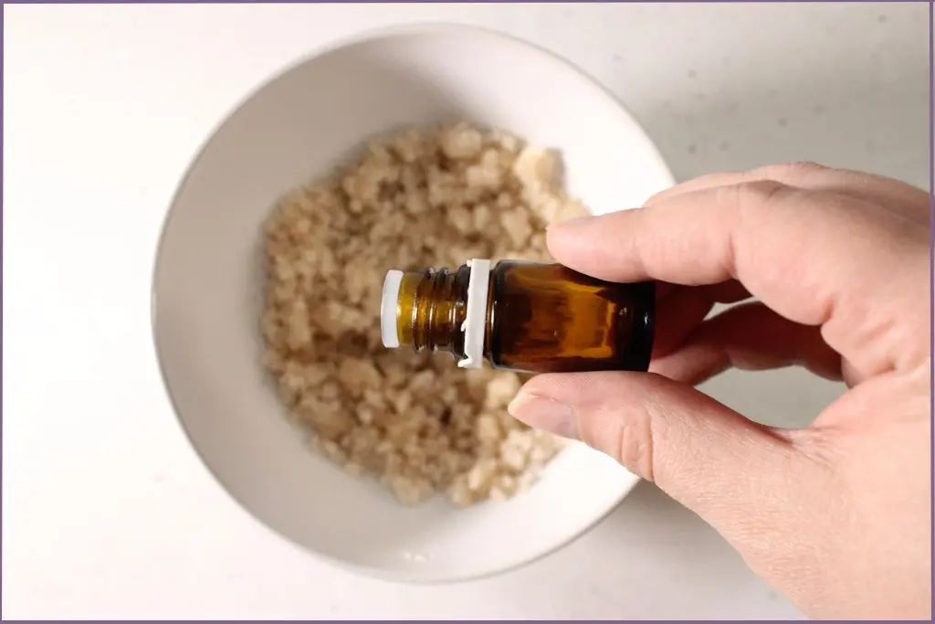 A person's hand putting essential oils in a homemade exfoliating foot scrub
