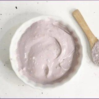 white bowl showing the end product of DIY clay face mask recipe with DIY Purple Brazilian clay mask with lavender. A wooden spoon with Brazilian clay is at the side