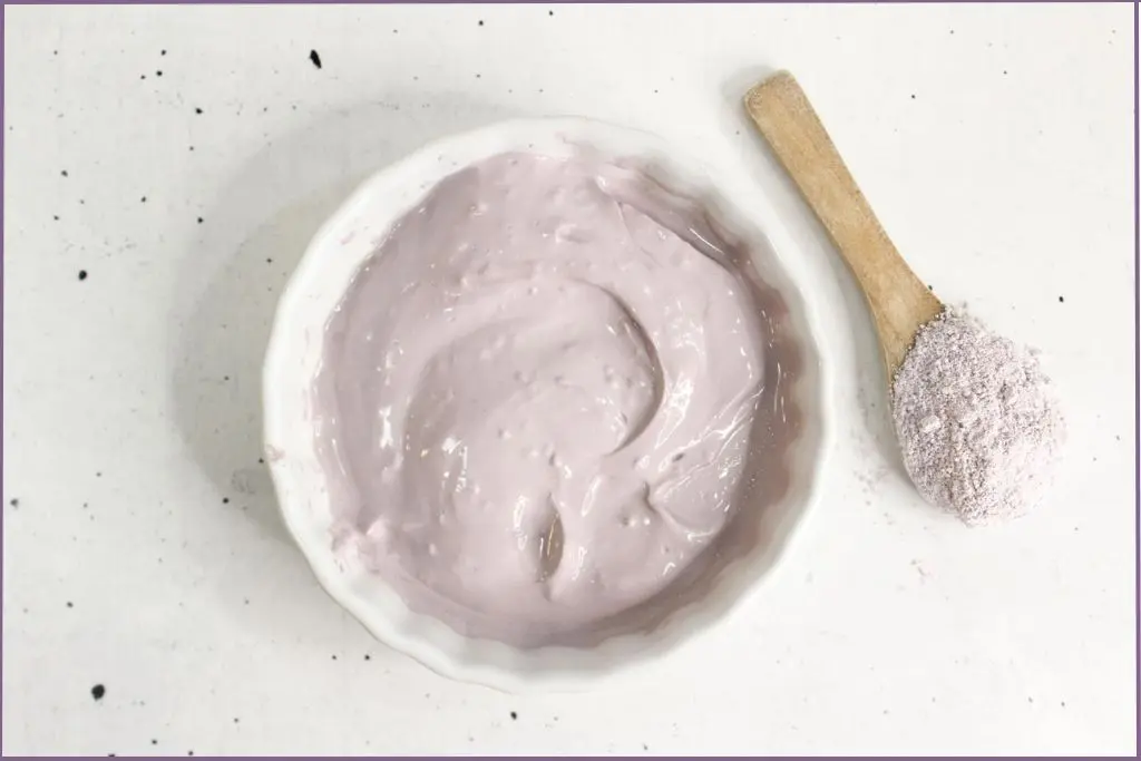 white bowl showing the end product of DIY clay face mask recipe with DIY Purple Brazilian clay mask with lavender. A wooden spoon with Brazilian clay is at the side