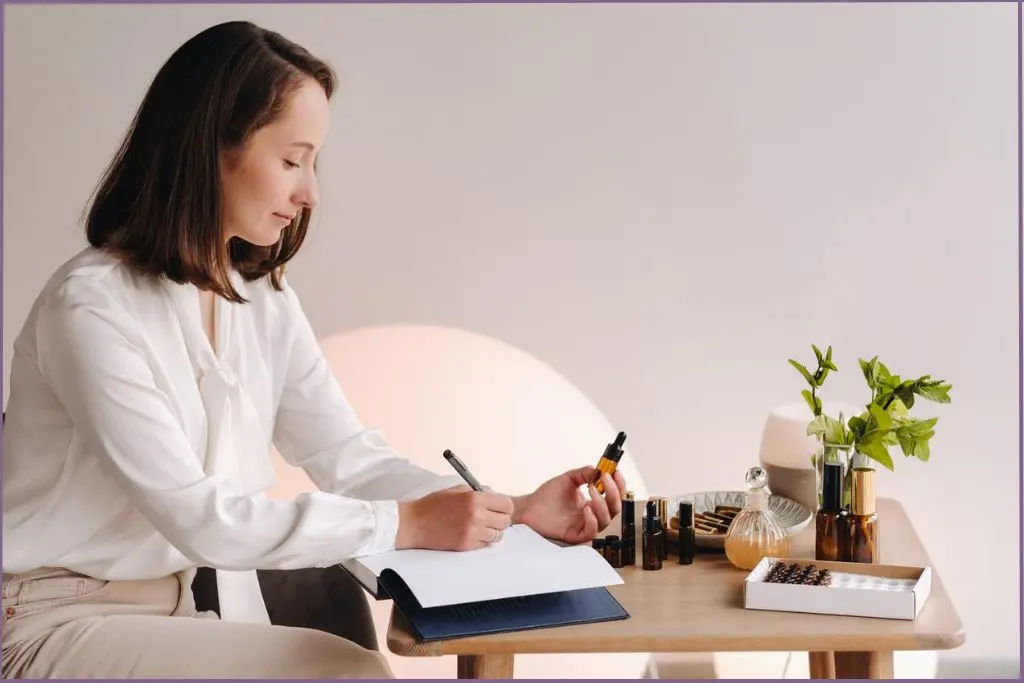 Aromatherapist holding an essential oil bottle in one hand and writing in an essential oil journal with her other hand.
