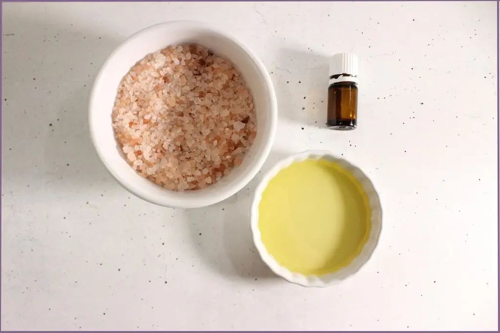 2 Glass bowls with Himalayan salt and carrier oil and an essential oil bottle - Ingredients for DIY exfoliating foot scrub with essential oils