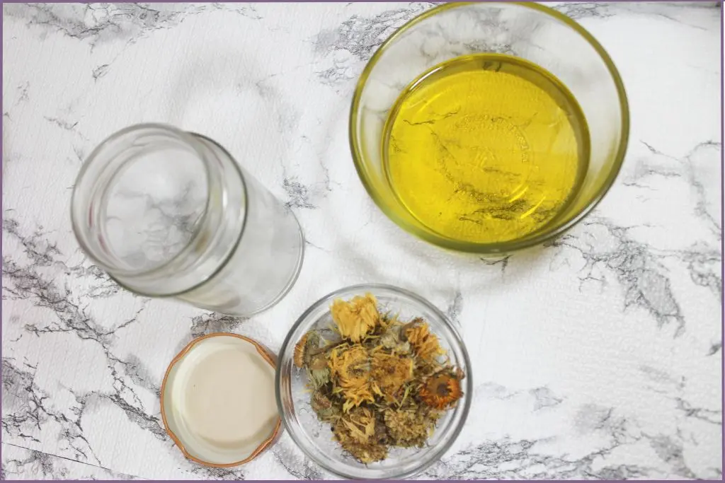 2 bowls with carrier oil and dried calendula flowers next to an empty glass jar to make calendula infused oil