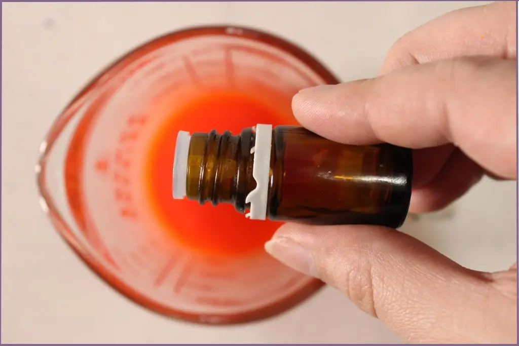 Pouring essential oil in melted, dyed soy wax to make fall scented soy candles with essential oils