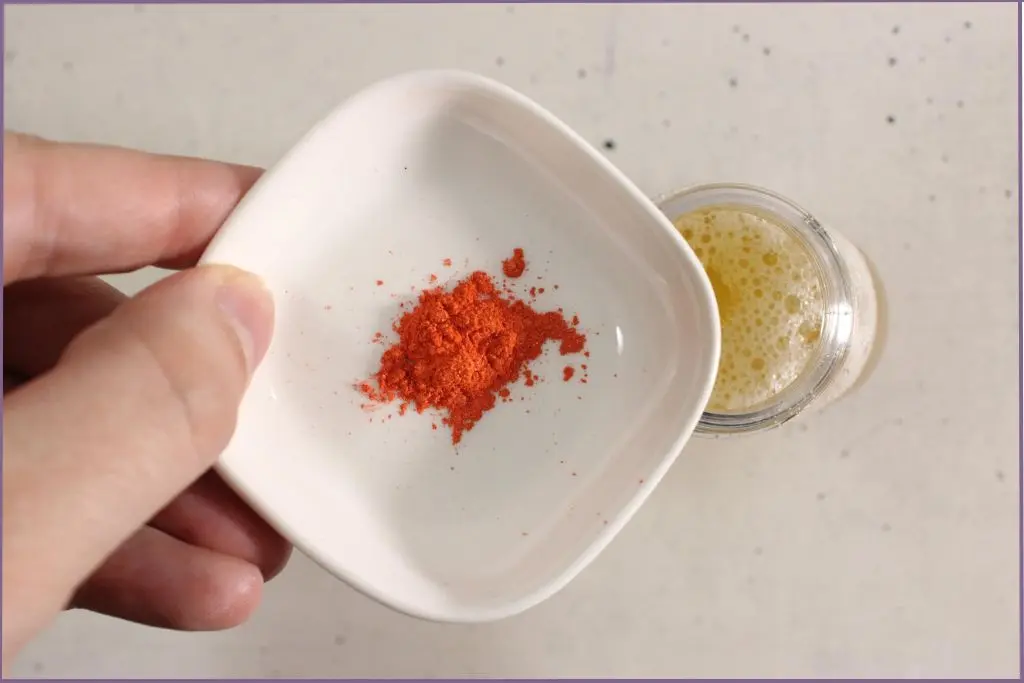 hand adding orange mica powder into hand soap mix to color homemade fall foaming hand soap