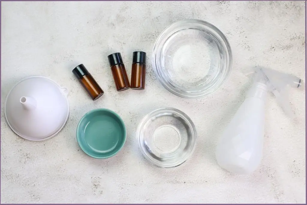 Ingredients for homemade fall room spray with essential oils - bowls with witch hazel, glycerin, and water, funnel and 3 essential oil bottles