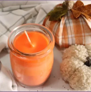 Orange colored DIY fall scented soy candle with fabric pumpkins at the side