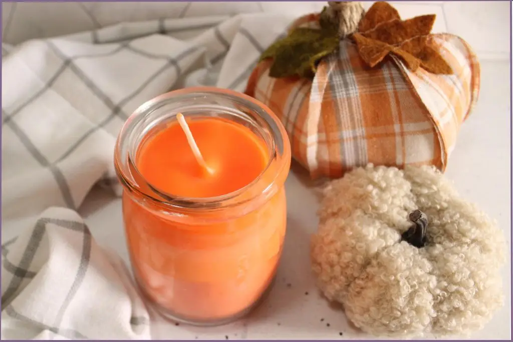 Orange colored DIY fall scented soy candle with fabric pumpkins at the side