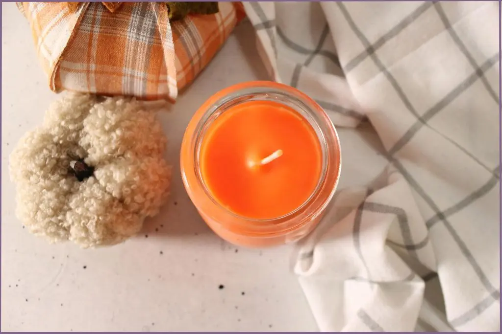 Orange colored DIY fall scented soy candle with fabric pumpkins at the side