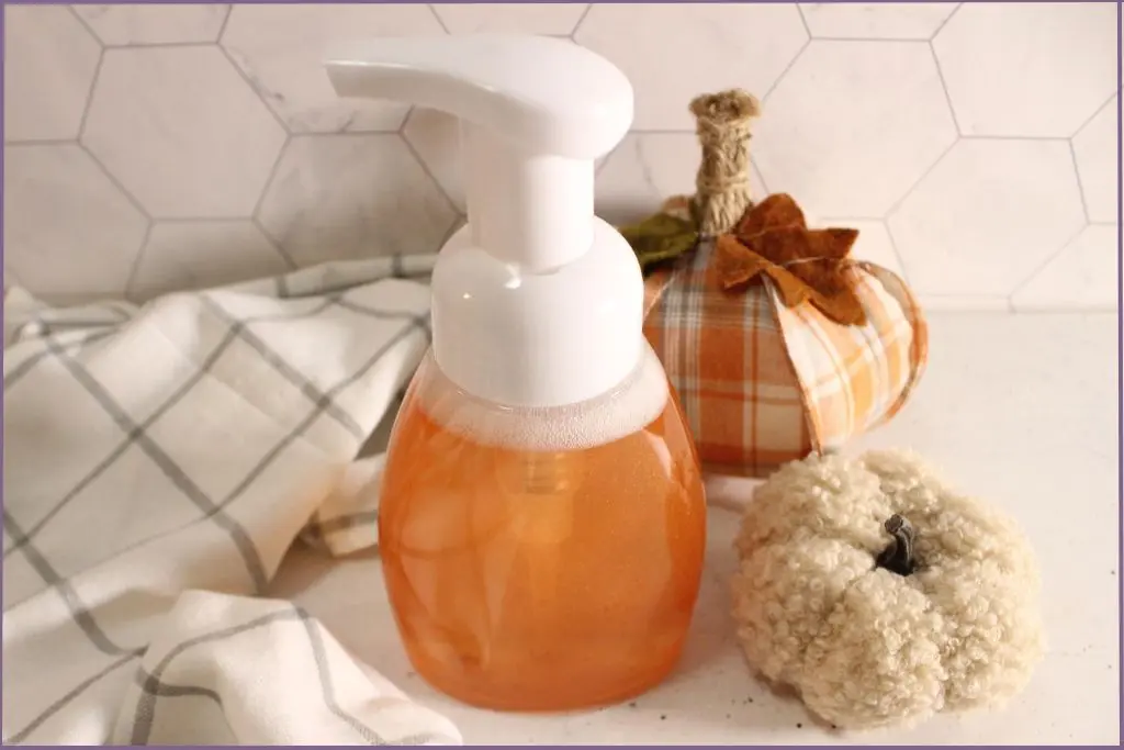 Pump bottle filled with DIY fall foaming hand soap with essential oils. Two fabric pumpkins lie on one side