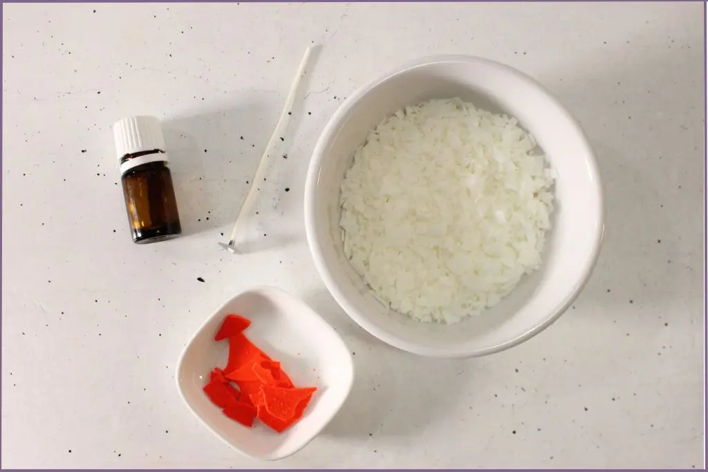 Ingredients for DIY fall scented soy candles with essential oils - Soy wax beads, orange candle dye, cotton wick, and essential oil bottle.