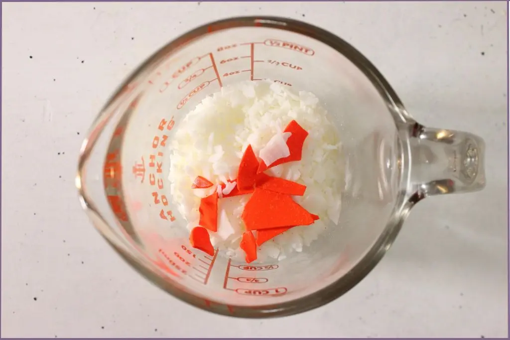 soy wax beads and orange candle dye in a glass measuring jar before melting to make fall scented soy candles