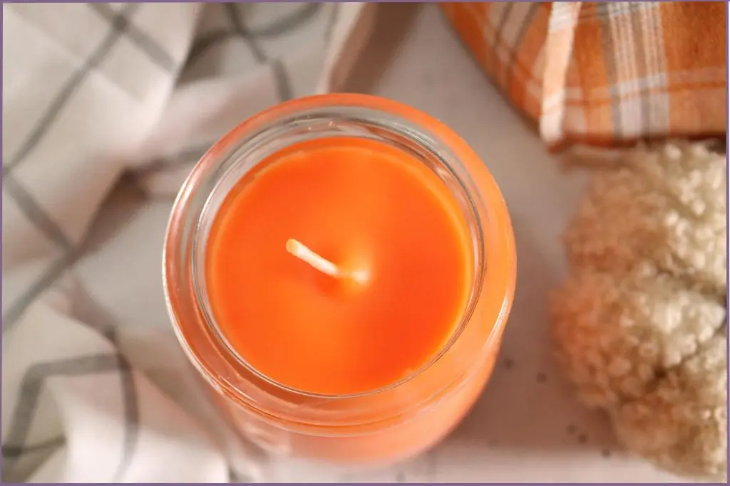 Orange colored DIY fall scented soy candle with fabric pumpkins at the side - Troubleshooting common candle making issues