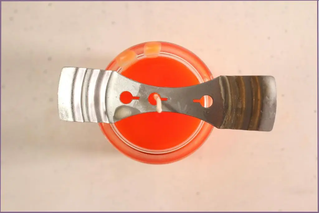 A metal wick holder holding the wick upright to make fall scented soy candle in a jar