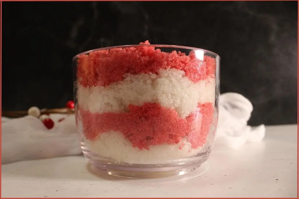 Alternating layers of red and white DIY candy cane sugar scrub in glass jar with tips on how to customize