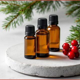 3 bottles of Christmas essential oils on round stone slap with pine and holly at the side
