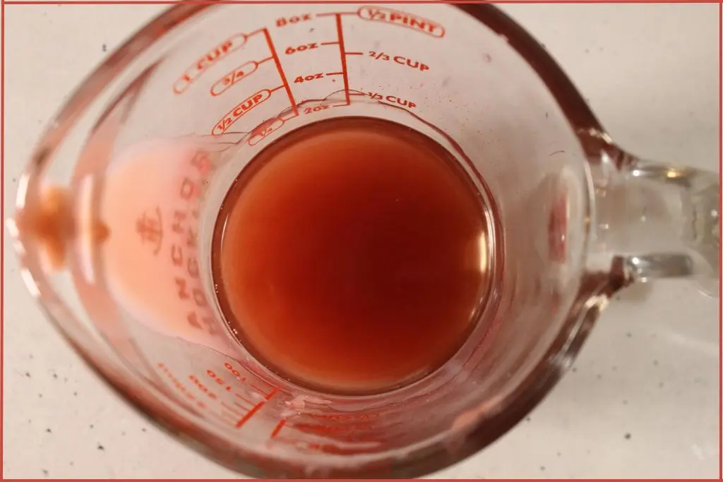 Glass measuring jar with melted red lip balm ingredients