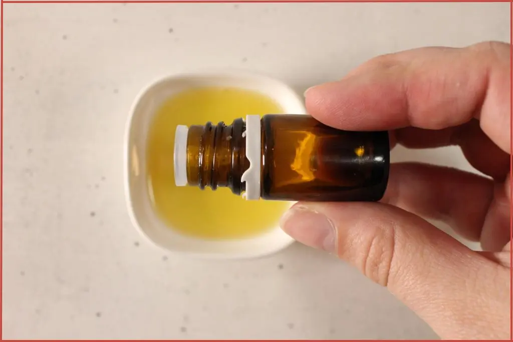pouring essential oil drops from a bottle into a white bowl with carrier oil to make Christmas roll-on perfume