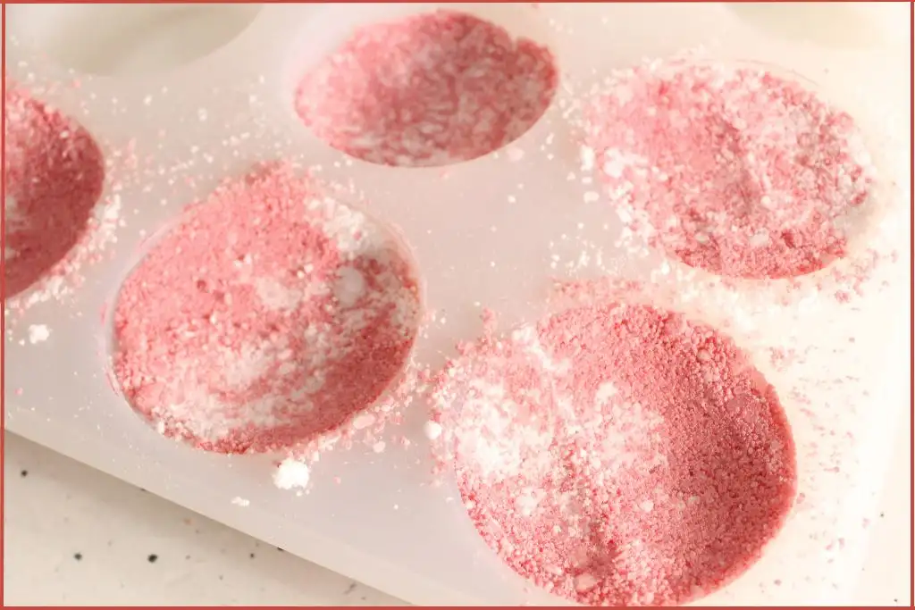 Silicone mold filled with red-and-white bath bomb mixture, showing the packing step of DIY candy cane bath bombs.