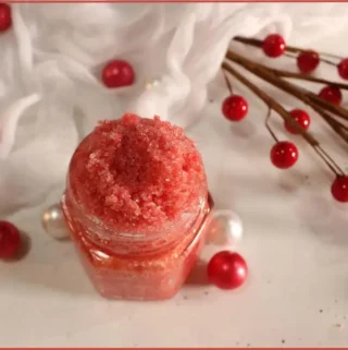 Finished candy cane lip scrub recipe in a small glass jar surrounded by white delicate fabric and red beads
