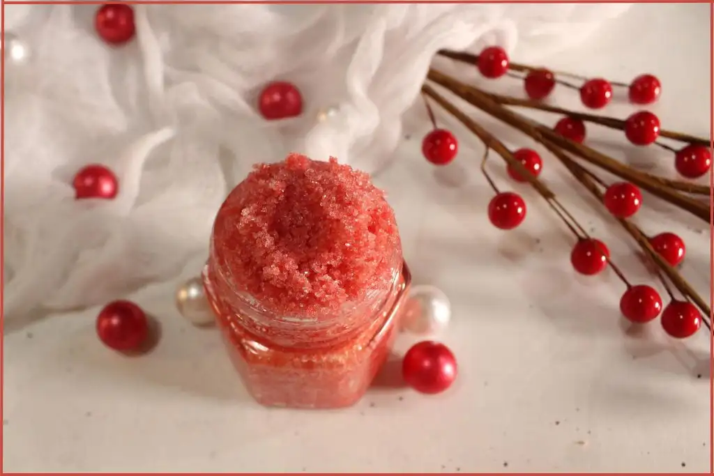 Finished candy cane lip scrub recipe in a small glass jar surrounded by white delicate fabric and red beads