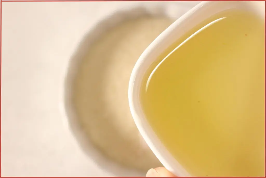 Pouring carrier oil and essential oil blend into bowl with brown sugar and Himalayan salt