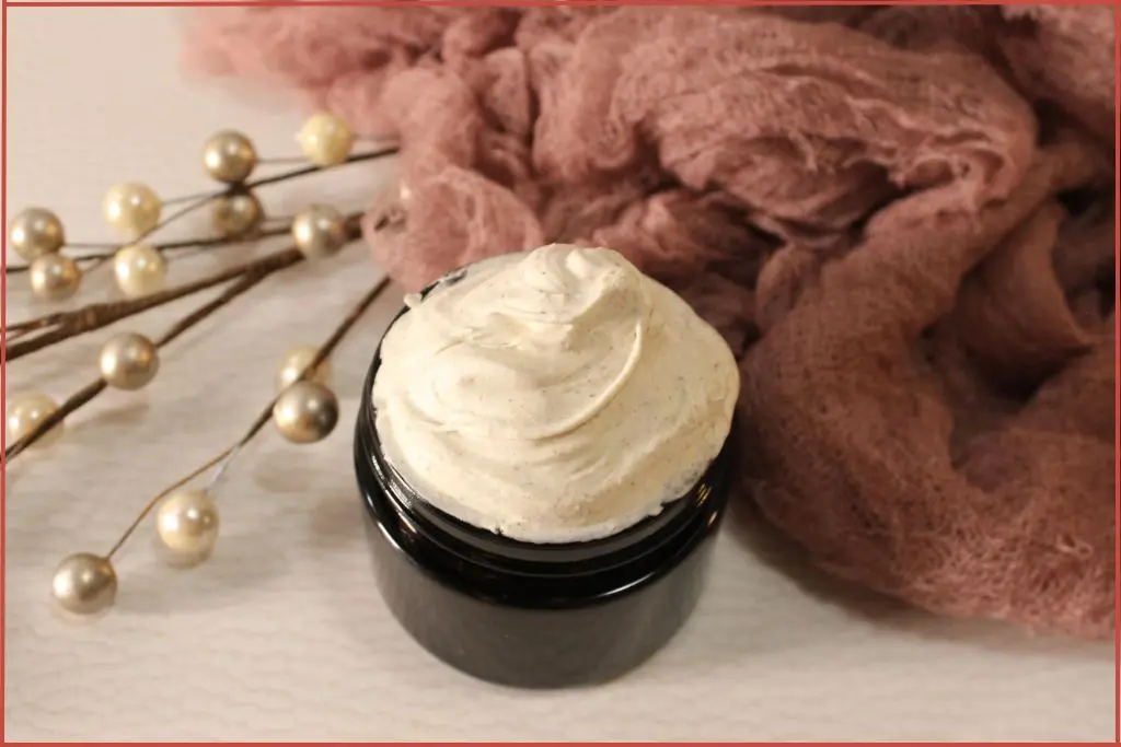 DIY gingerbread whipped body butter in a glass jar, creamy swirls on top, surrounded by soft pink cloth, and holiday pearl stems on a white background.