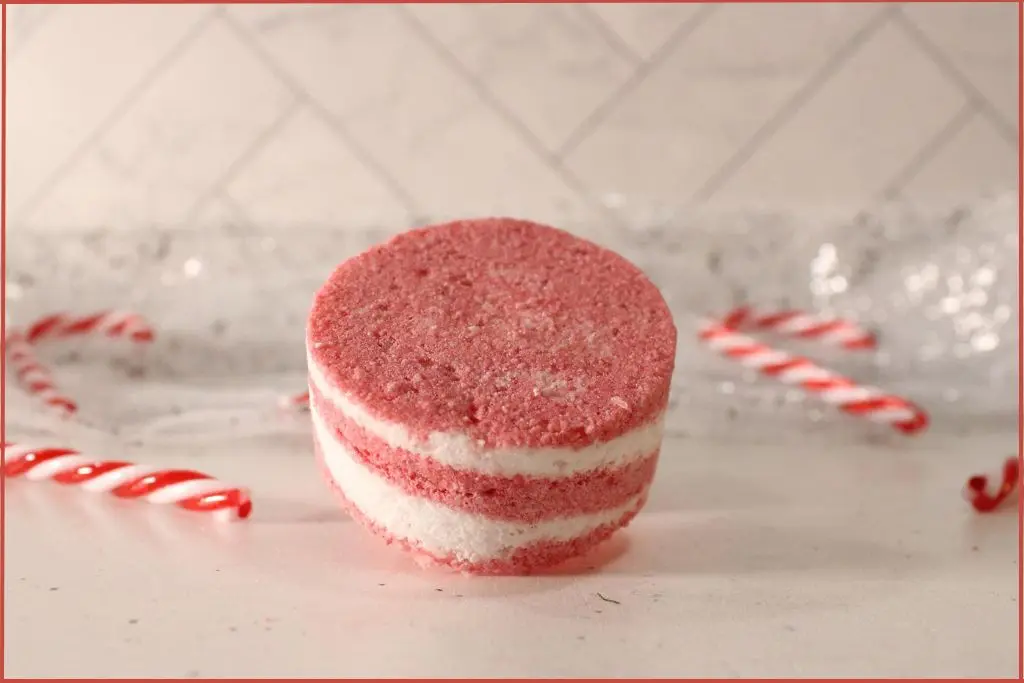 One round red-and-white layered candy cane bath bomb on a countertop, styled with mini candy canes with gifting ideas