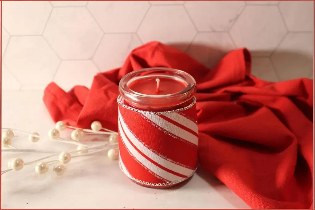 Red candle in a glass jar wrapped with red and white festive fabric demonstrating presentation ideas for a homemade candy cane candle