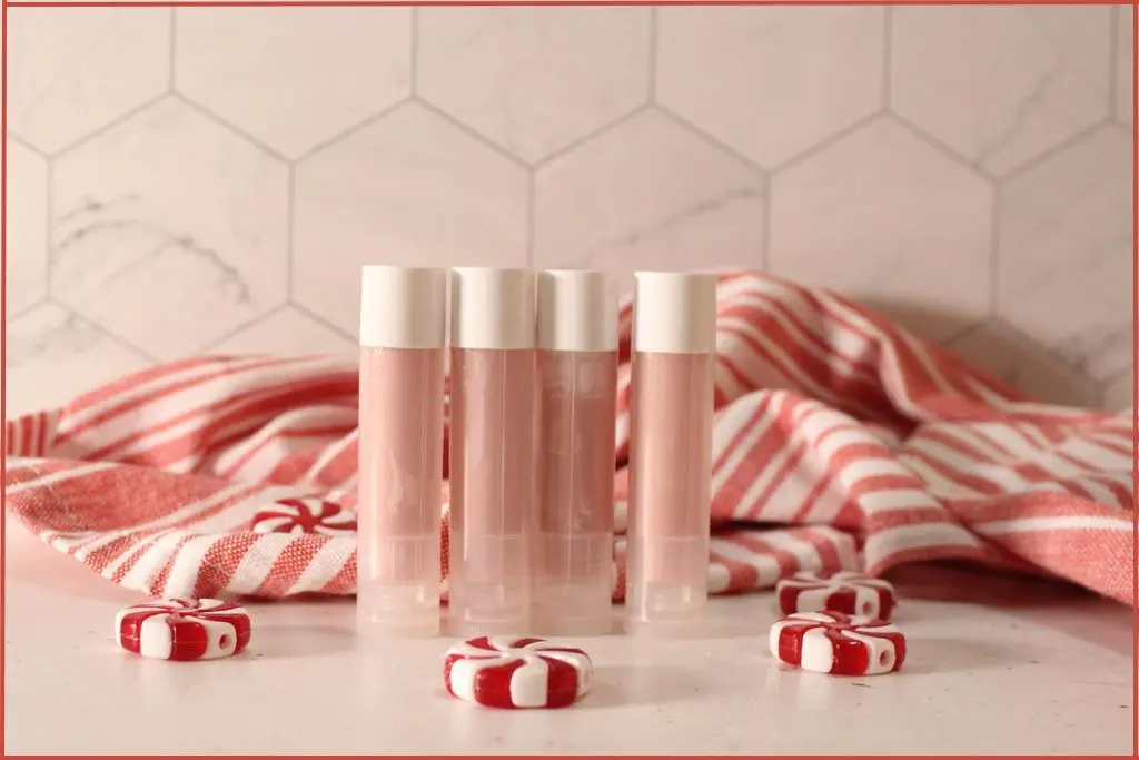 Customization ideas for four DIY candy cane lip balm tubes in front of a red‑and‑white striped towel, with peppermint candies scattered around.
