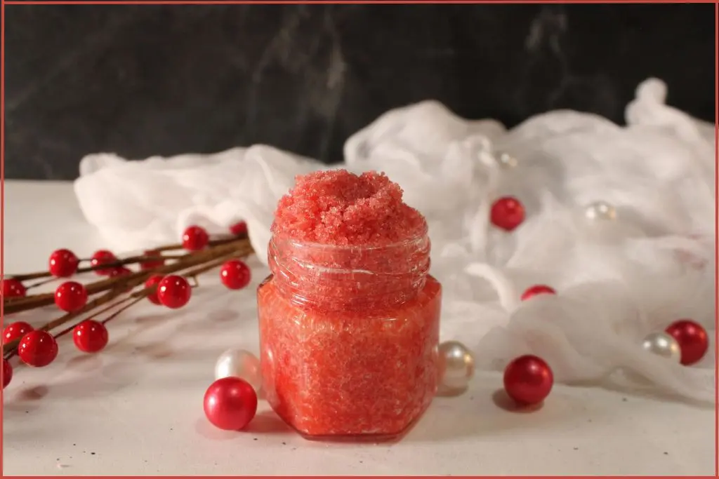 Homemade candy cane lip scrub in a small glass jar surrounded by white delicate fabric and red beads